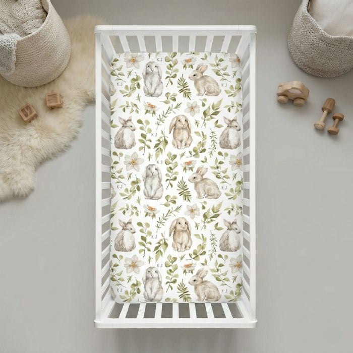 Drap housse lit bébé lapinou avec motifs lapins blancs aquarelle et feuillages verts dans lit à barreaux blanc