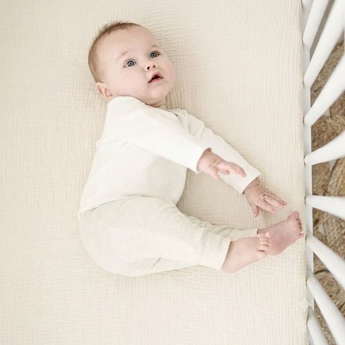 bébé allongé sur le coté sur drap housse bébé gaze de coton écru tout doux dans lit à barreaux