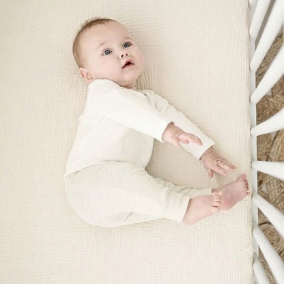 bébé allongé sur le coté sur drap housse bébé gaze de coton écru tout doux dans lit à barreaux
