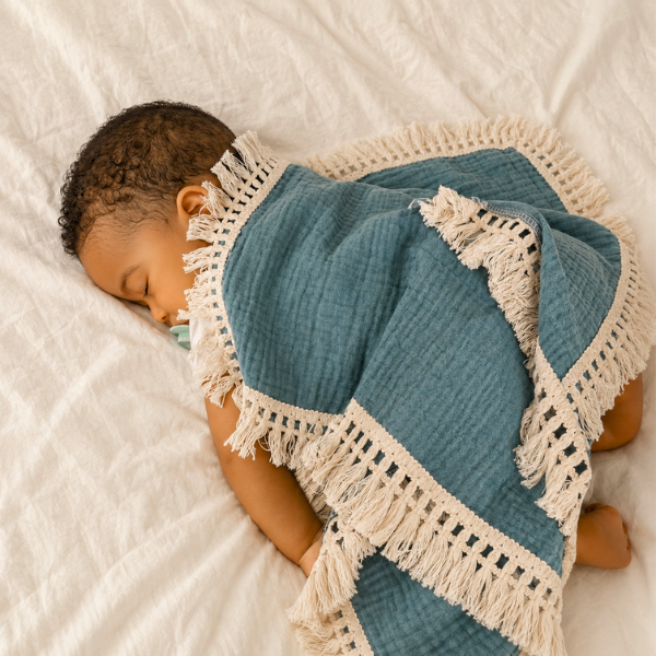 bebe-dort-sur-le-ventre-couvert-par-couverture-bebe-en-mousseline-a-frange-bleu-uni