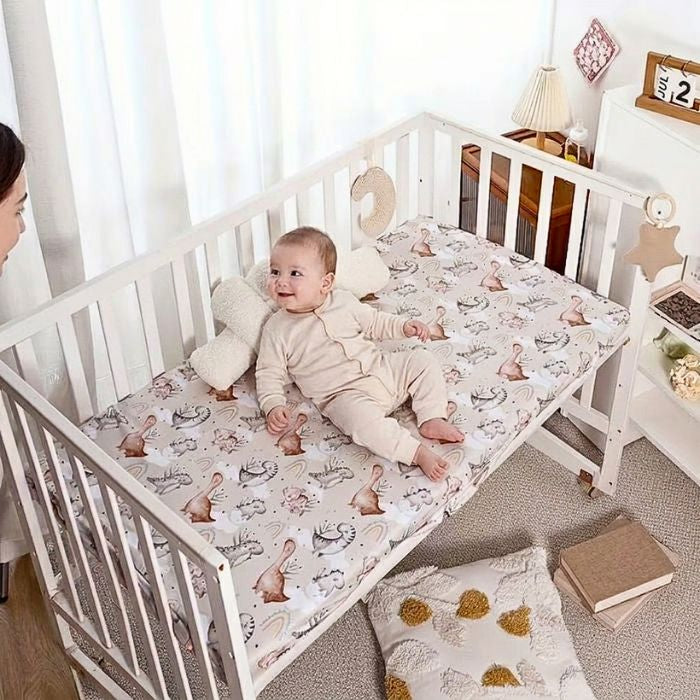 bébé souriant regardant vers sa maman allongé sur drap housse lit bébé dino  