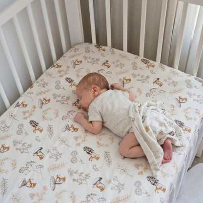 Bébé endormi sur le ventre sur un drap housse bebe motif forêt et lapins dans un lit à barreaux blanc
