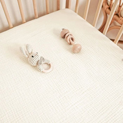 drap housse bébé gaze de coton écru tout doux avec deux jouets dans lit à barreaux