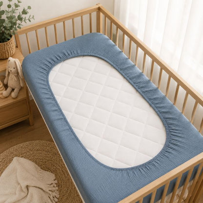drap housse lit bébé gaze de coton bleu retourné avec élastiques dans lit à barreaux bois