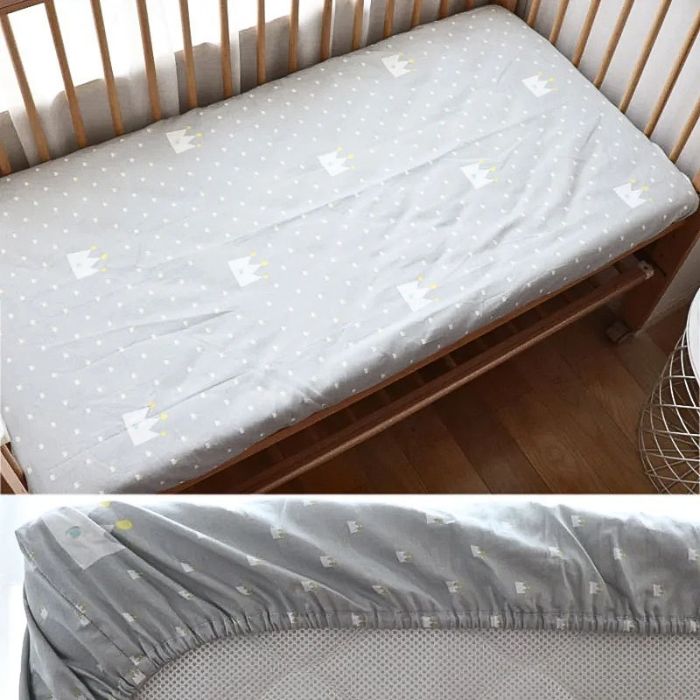 drap housse bebe couronne blanche sur fond gris avec elastique pose sur lit a barreaux en bois naturel