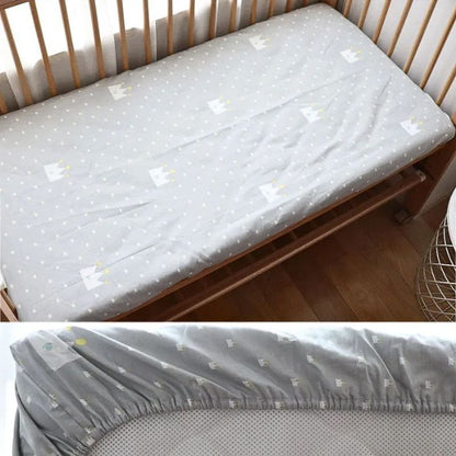 drap housse bebe couronne blanche sur fond gris avec elastique pose sur lit a barreaux en bois naturel