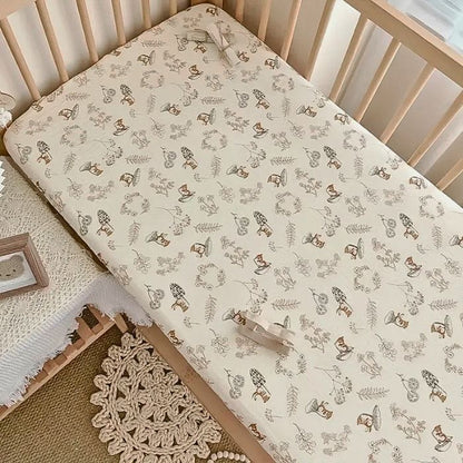 Drap housse bébé motif forêt et lapins posé sur lit à barreaux en bois naturel, écureuils, champignons et botaniques aux tons caramel et brun